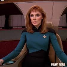 Beverly Crusher seated in the captain's chair on the Enterprise-D bridge.