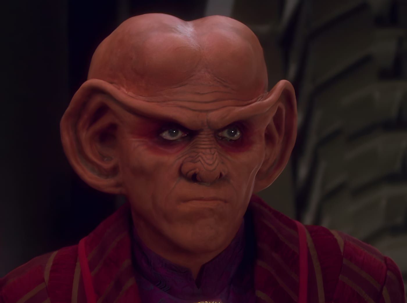 Close-up of a Ferengi male with large ears and a severe, calculating expression.