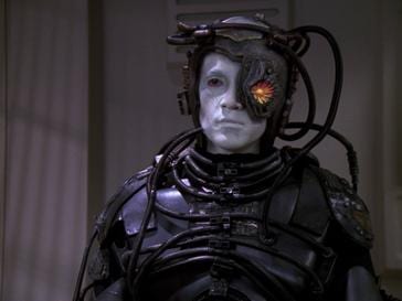 Hugh in full Borg drone implants and armor with an illuminated ocular device.