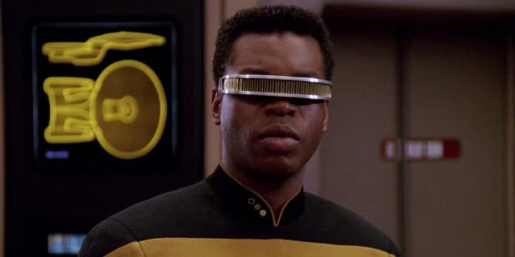 Geordi La Forge in a Starfleet operations uniform, looking toward an engineering problem.