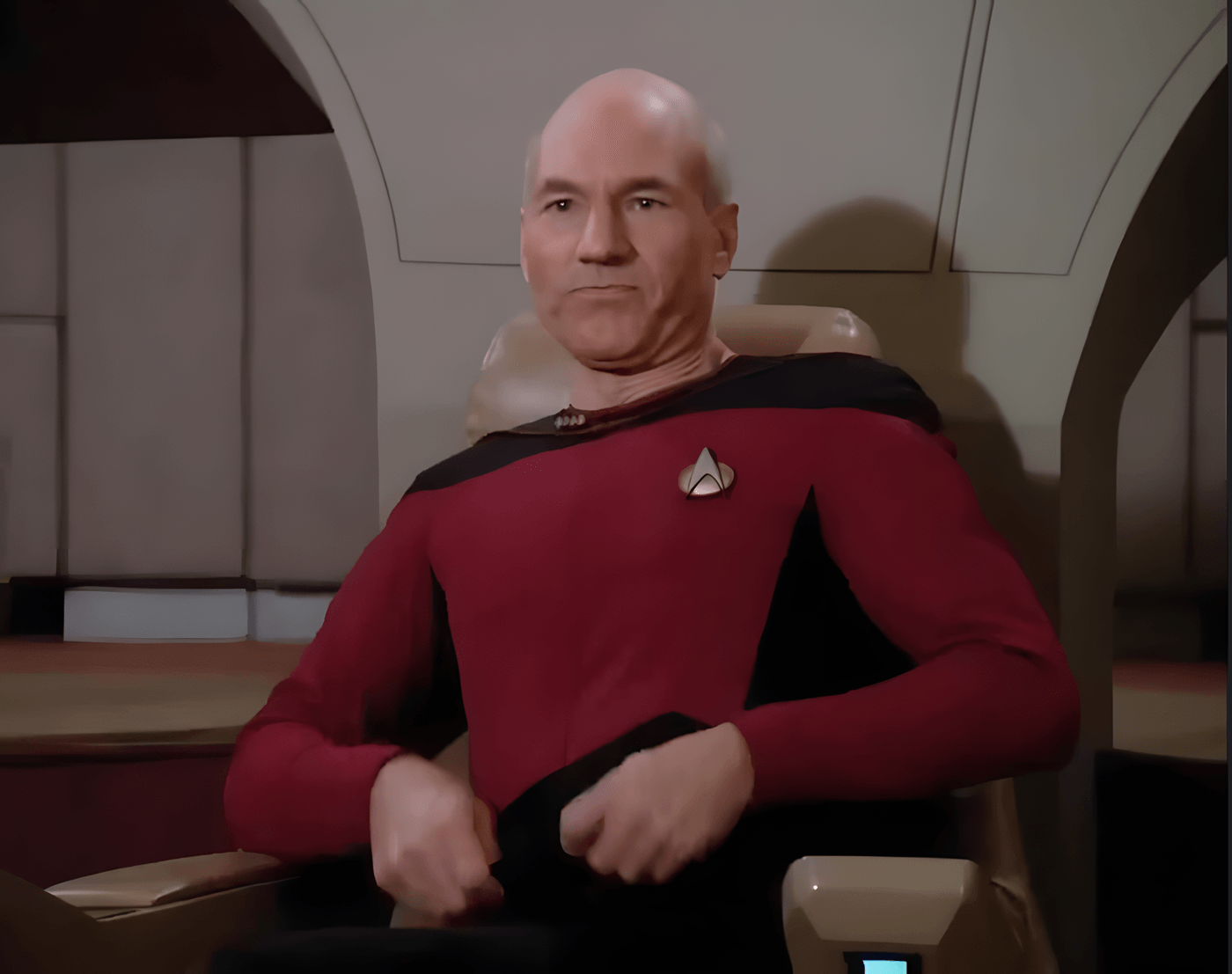 Captain Picard on the Enterprise-D bridge, seated in the command chair, tugging his red uniform tunic straight with both hands.