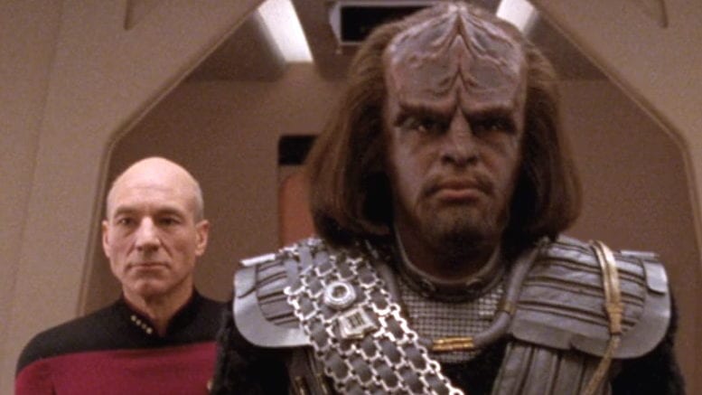 Jean-Luc Picard standing behind Worf in Klingon armor.