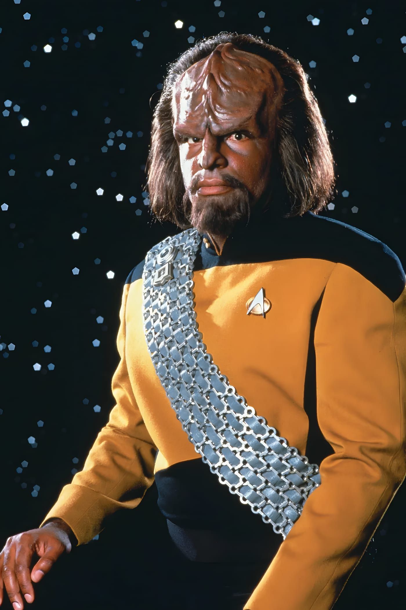 Worf standing in a gold Starfleet uniform and Klingon baldric.